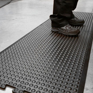 Person standing on textured anti-fatigue mat with raised circles, providing cushioning and slip resistance