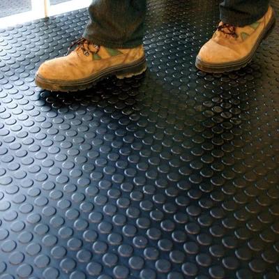 Brown boots standing on a black studded rubber flooring roll in a gym or industrial area, showing non‑slip texture.