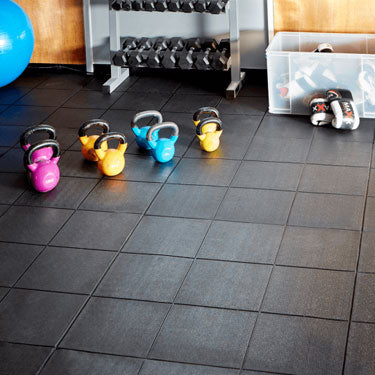 Kettlebells on interlocking gym floor tiles with storage boxes in a home gym