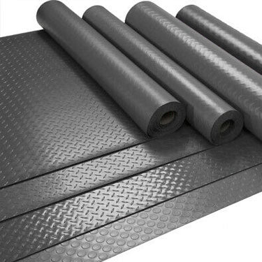 Rolls of black rubber matting with textured ribbed and studded surfaces