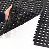 Hands lifting corner of Slip-Not hollow ring interlocking drainage rubber mat tile; close-up of open ring matting showing ring holes and interlocking edges, heavy-duty natural rubber tile measuring 0.91 m x 0.91 m and 15 mm thick for drainage, anti-slip and anti-fatigue support
