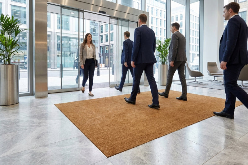 Coir entrance matting set into recessed matwell at UK office building — flush floor installation with natural brown coconut fibre surface