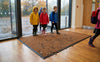 Brown waffle absorbent entrance mat at UK primary school — wet rainy entrance, children with muddy boots, waffle grid surface working
