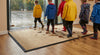 Oat cream waffle absorbent entrance mat at UK school — rainy day, children with wellington boots, waffle grid trapping mud and water