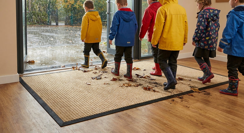 Oat cream waffle absorbent entrance mat at UK school — rainy day, children with wellington boots, waffle grid trapping mud and water