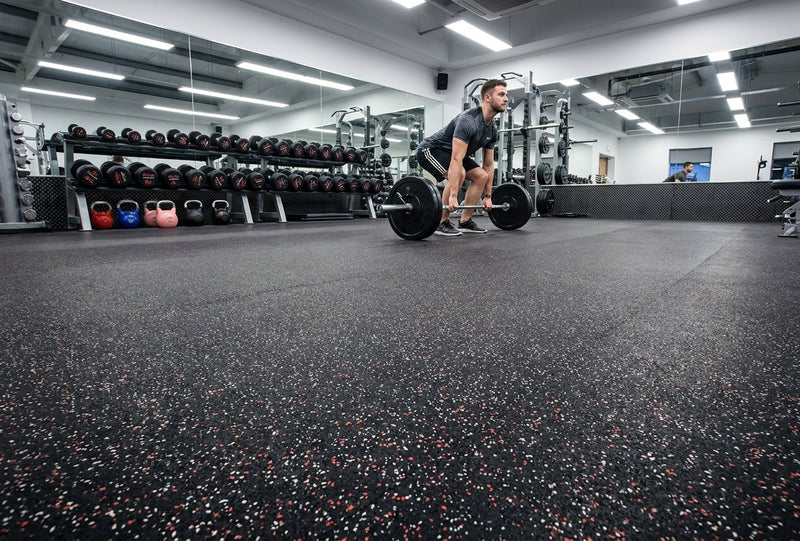 Black rubber gym matting roll installed in commercial weight room — 1.25m x 10m seamless roll, deadlift in progress