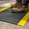 Black anti-fatigue mats in pebble and ribbed textures — 9mm foam, bevelled trip-resistant edges, yellow safety border option