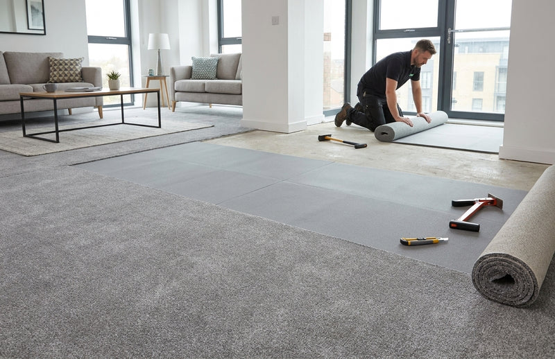 Carpet fitter installing memory foam underlay in modern UK flat — showing subfloor to underlay to finished carpet progression in one shot