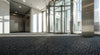 Anthracite ribbed entrance carpet matting in luxury corporate building with glass revolving door — premium dark grey polypropylene cut-and-loop pile, 12mm thick, rubber waffle backed