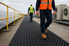 Heavy-duty open ring roof matting walkway with worker walking on rooftop; non-slip durable rubber matting features raised rings and open-grid design for drainage and traction, protecting roof membranes and providing safe walkway across wet areas. Mats measure 22 mm thick and are made from weather-resistant rubber.