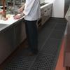 Chef standing on Slip-Not hollow ring interlocking drainage rubber mats in a commercial kitchen; open ring pattern allows liquids to drain through, heavy-duty natural rubber matting measuring 0.91 m x 0.91 m and 15 mm thick, providing anti-fatigue support and slip resistance in wet areas