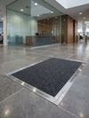 Silver chrome matwell frame installed flush in commercial building entrance — coir mat inside, flush with surrounding stone floor, professional finish