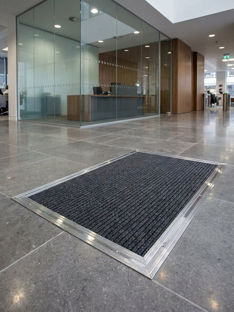 Silver chrome matwell frame installed flush in commercial building entrance — coir mat inside, flush with surrounding stone floor, professional finish